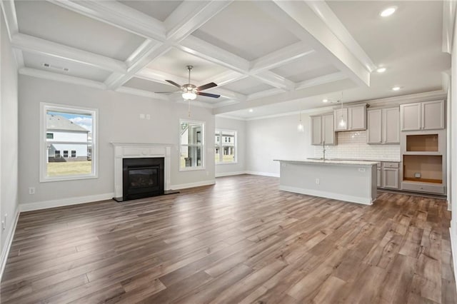 unfurnished living room featuring coffered ceiling, beam ceiling, wood-type flooring, ornamental molding, and ceiling fan