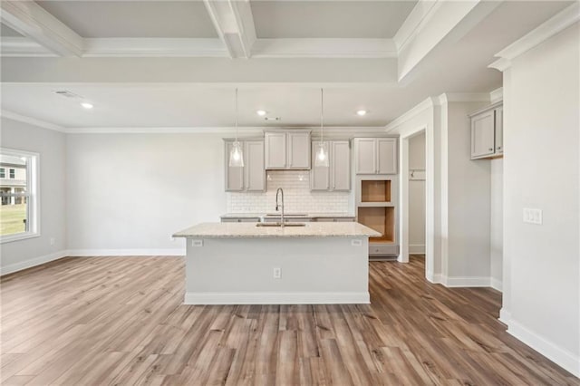 kitchen featuring sink, hanging light fixtures, hardwood / wood-style floors, light stone counters, and a kitchen island with sink