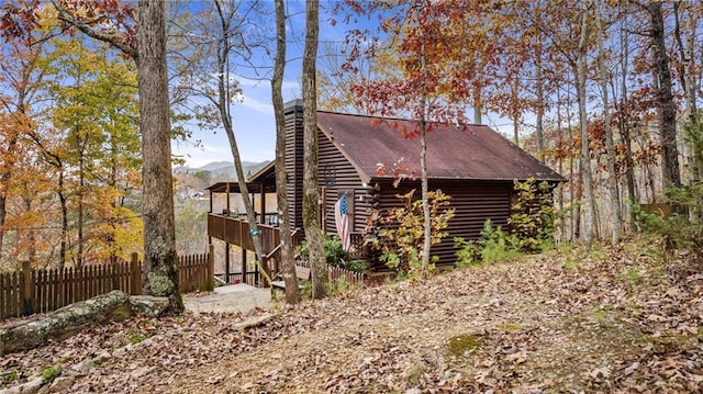 view of side of home with a chimney, log siding, a mountain view, and fence