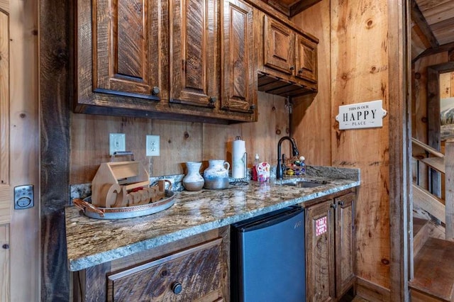 kitchen featuring stainless steel fridge, stone counters, sink, and wood walls