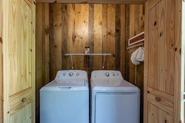 clothes washing area featuring washing machine and clothes dryer and wooden walls