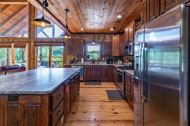 kitchen featuring appliances with stainless steel finishes, vaulted ceiling, pendant lighting, light hardwood / wood-style flooring, and a kitchen island