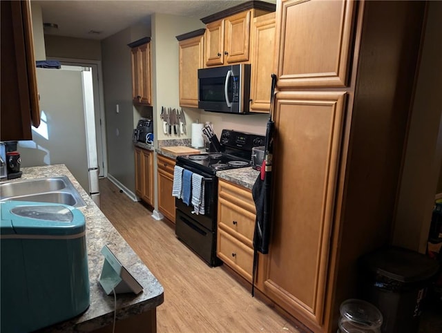 kitchen featuring freestanding refrigerator, stainless steel microwave, a sink, light wood finished floors, and black / electric stove