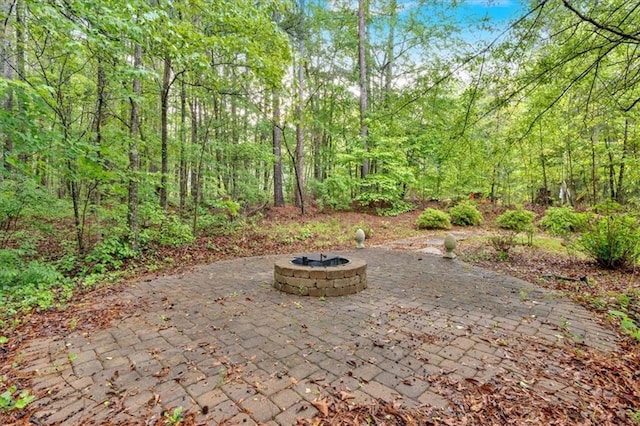 view of patio with an outdoor fire pit and a wooded view