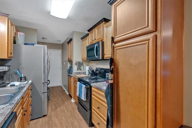 kitchen featuring a textured ceiling, stainless steel appliances, light wood-style flooring, and a sink