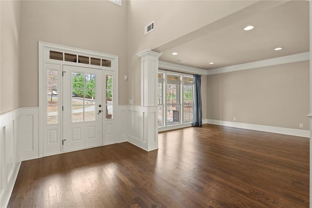 entryway featuring healthy amount of natural light, wainscoting, decorative columns, crown molding, and dark wood-style floors