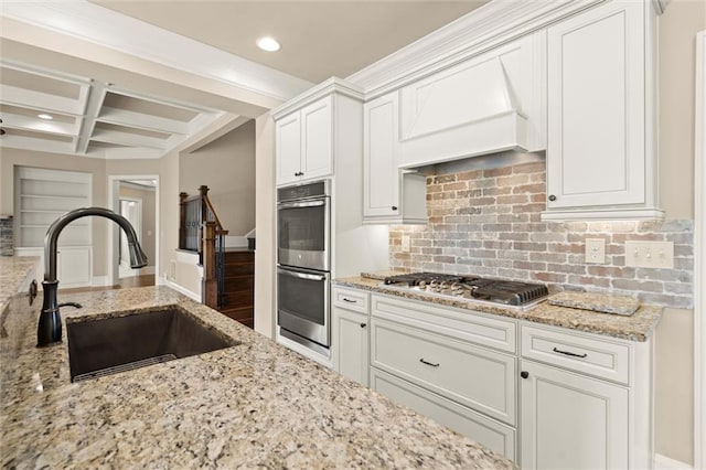 kitchen featuring appliances with stainless steel finishes, a sink, coffered ceiling, tasteful backsplash, and beam ceiling