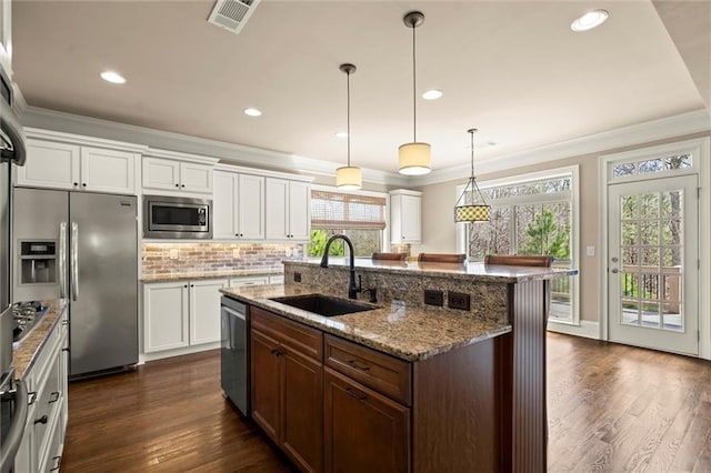 kitchen with appliances with stainless steel finishes, a sink, ornamental molding, an island with sink, and dark wood finished floors