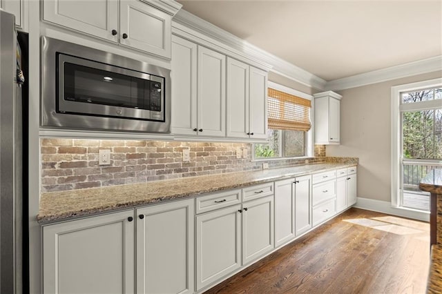 kitchen featuring stainless steel microwave, baseboards, ornamental molding, wood finished floors, and backsplash