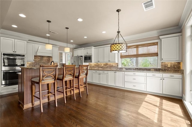 kitchen with stainless steel appliances, crown molding, backsplash, a kitchen breakfast bar, and custom range hood