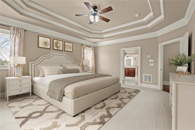 bedroom featuring a tray ceiling, crown molding, carpet, ceiling fan, and connected bathroom