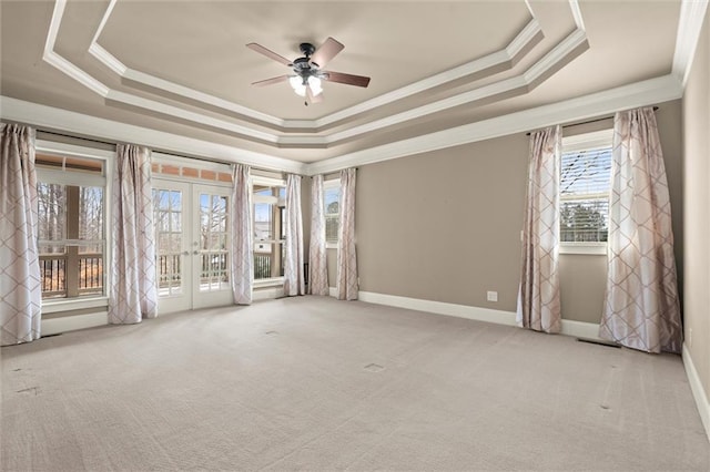 carpeted empty room with french doors, ornamental molding, a tray ceiling, a ceiling fan, and baseboards