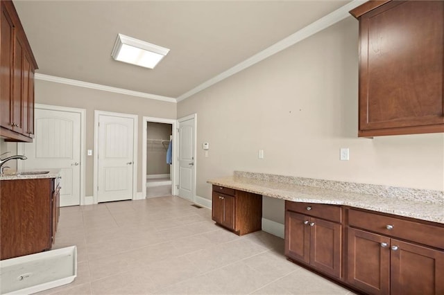 kitchen with a sink, ornamental molding, baseboards, light tile patterned floors, and light stone counters