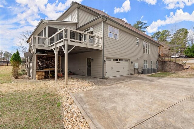 back of property featuring an attached garage, a deck, concrete driveway, and cooling unit