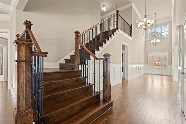 stairs with a chandelier, wood finished floors, ornamental molding, a high ceiling, and a wainscoted wall
