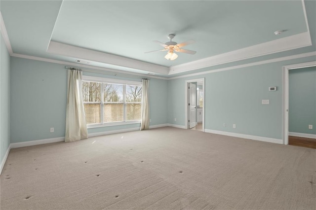 carpeted empty room with a tray ceiling, ceiling fan, baseboards, ornamental molding, and a smoke detector