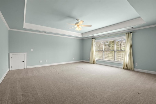 carpeted empty room with a tray ceiling, a ceiling fan, ornamental molding, and baseboards