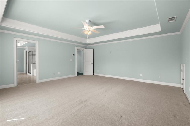 unfurnished bedroom featuring a raised ceiling, light carpet, ornamental molding, baseboards, and ceiling fan