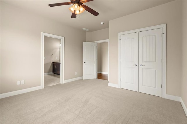 unfurnished bedroom featuring light colored carpet, a closet, ensuite bath, and ceiling fan