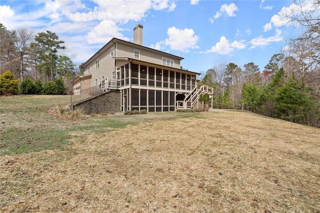 back of property with a sunroom, stairs, a chimney, and a lawn