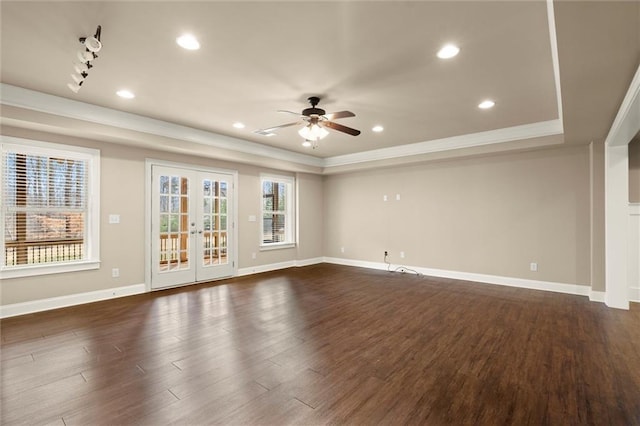 unfurnished living room with a tray ceiling, ceiling fan, dark wood-type flooring, ornamental molding, and baseboards