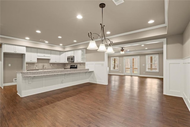 kitchen with ornamental molding, stainless steel microwave, wainscoting, a peninsula, and white cabinets