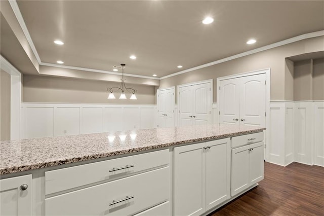kitchen featuring a wainscoted wall, white cabinetry, a decorative wall, light stone countertops, and ornamental molding