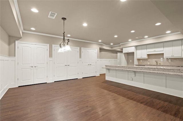 kitchen featuring a decorative wall, crown molding, wainscoting, light stone countertops, and a breakfast bar area