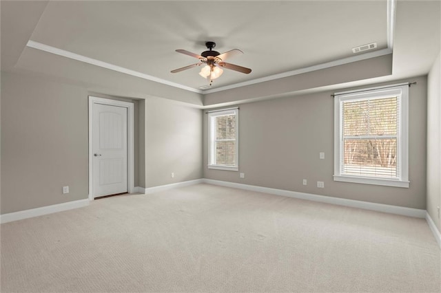 spare room with a raised ceiling, ceiling fan, light carpet, baseboards, and ornamental molding