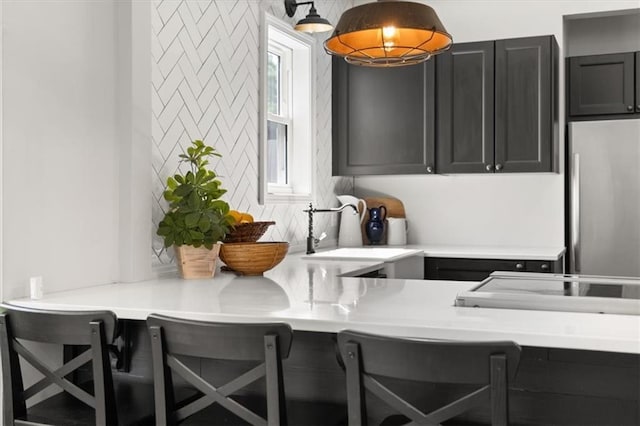 kitchen featuring a kitchen breakfast bar, stainless steel refrigerator, sink, and hanging light fixtures