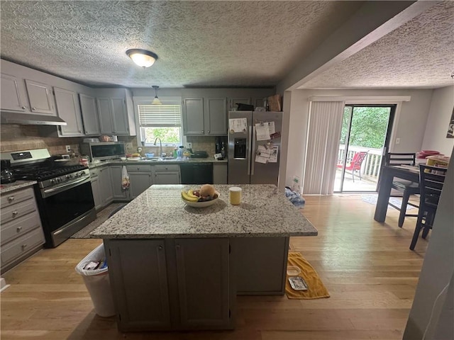 kitchen with stainless steel appliances, a center island, light wood finished floors, a textured ceiling, and tasteful backsplash