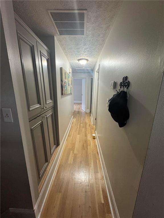 hallway with a textured ceiling and light wood-style flooring