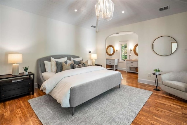 bedroom featuring a notable chandelier, wood finished floors, visible vents, and baseboards