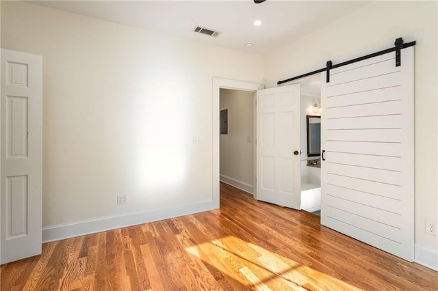 spare room with a barn door, visible vents, baseboards, light wood-style floors, and electric panel