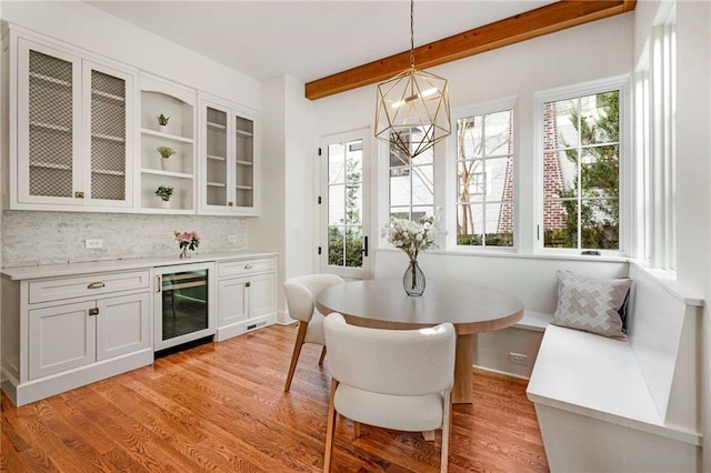 dining room with light wood-style floors, beverage cooler, breakfast area, and beam ceiling