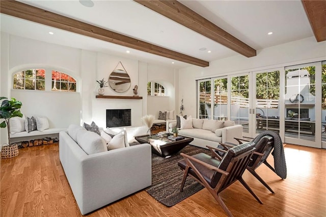 living room featuring plenty of natural light, light wood-type flooring, a fireplace, and beam ceiling