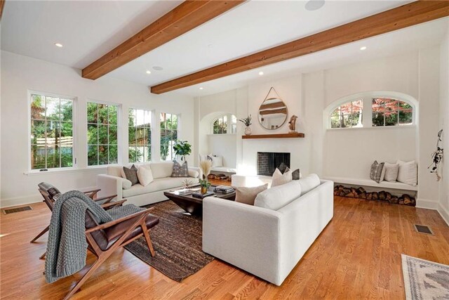 living area with a fireplace, visible vents, a healthy amount of sunlight, light wood finished floors, and beamed ceiling