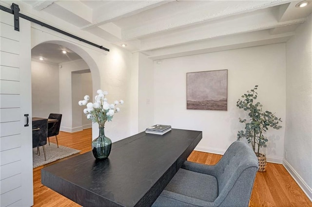 office area featuring arched walkways, a barn door, wood finished floors, baseboards, and beamed ceiling