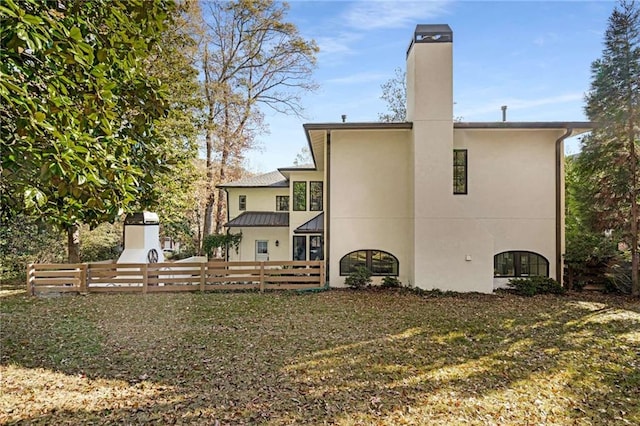 rear view of house featuring a lawn, fence, a chimney, and stucco siding