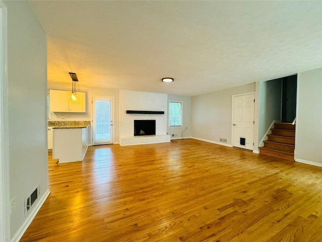 3210 Ebenezer Rd, Marietta, GA 30066 - unfurnished living room featuring light wood-style flooring, a brick fireplace, baseboards, stairway, and a textured ceiling