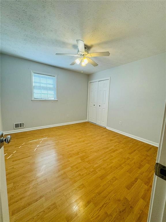 3210 Ebenezer Rd, Marietta, GA 30066 - unfurnished bedroom with light wood-type flooring, a textured ceiling, baseboards, a closet, and ceiling fan