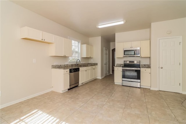 kitchen featuring stainless steel appliances, dark stone counters, white cabinets, sink, and light tile patterned flooring