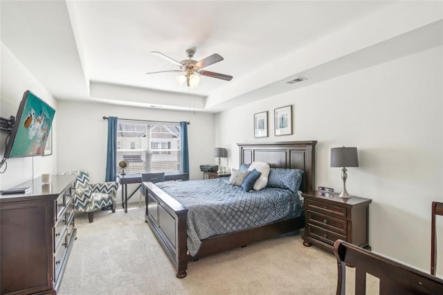 bedroom with light carpet, a raised ceiling, visible vents, and a ceiling fan