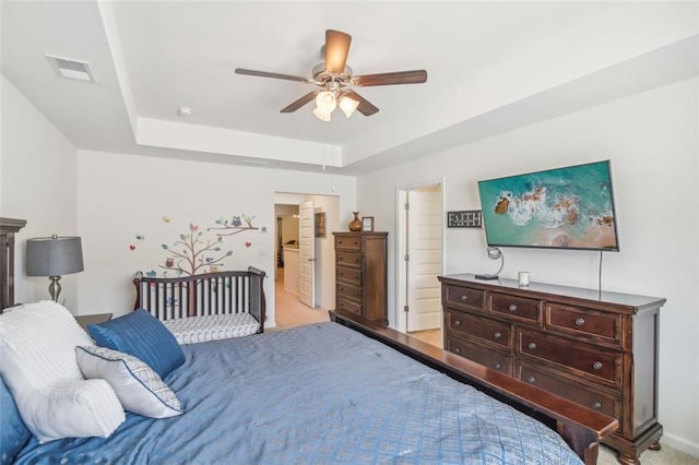 bedroom featuring a raised ceiling, visible vents, ceiling fan, and ensuite bathroom