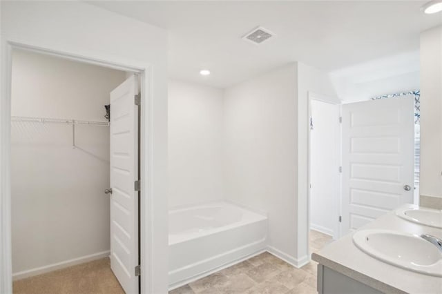 bathroom with a bathing tub, a sink, visible vents, baseboards, and a spacious closet