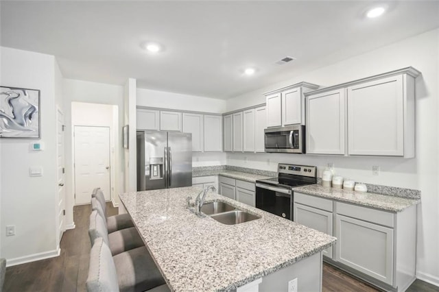 kitchen with a sink, visible vents, appliances with stainless steel finishes, dark wood-style floors, and a kitchen bar