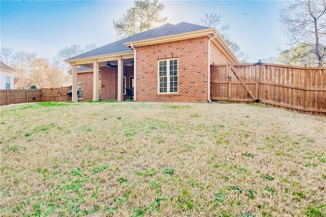 back of property with ceiling fan, a fenced backyard, brick siding, a yard, and a gate