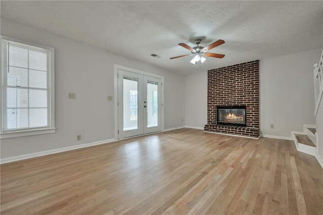 unfurnished living room with french doors, light hardwood / wood-style floors, a textured ceiling, ceiling fan, and a fireplace