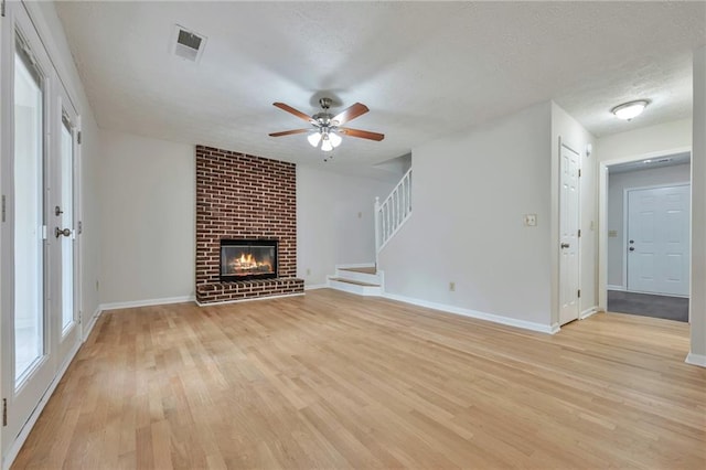 unfurnished living room with a brick fireplace, light hardwood / wood-style flooring, a textured ceiling, and ceiling fan