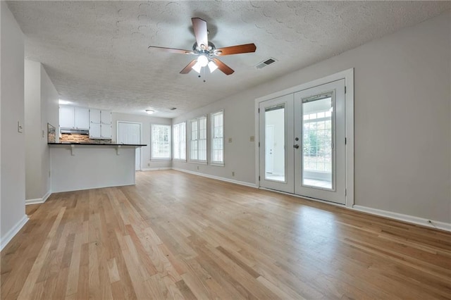 unfurnished living room featuring light hardwood / wood-style floors, plenty of natural light, a textured ceiling, and french doors